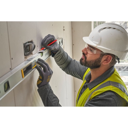 Photo of worker using STANLEY FMHT43676-1 spirit level against wall, wearing gloves and helmet.
