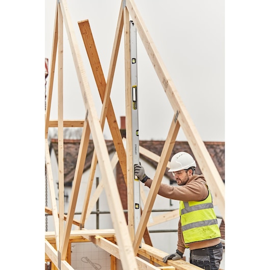 STANLEY FMHT43679-1 spirit level used vertically by a worker on a wooden roof frame at a construction site.