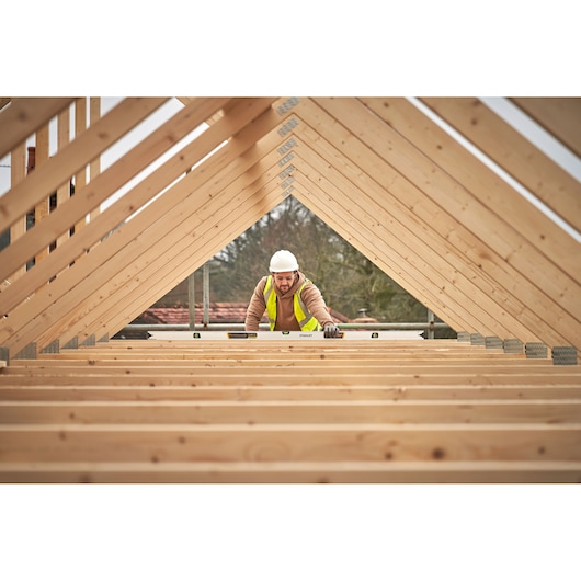 STANLEY FMHT43680-1 spirit level in use on wooden roof frame, worker wearing safety vest and helmet.
