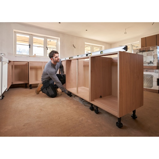 Stanley FMHT43680-1 spirit level used on kitchen cabinets, side angle, worker adjusting cabinet legs.