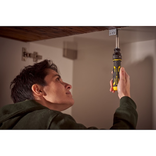 STANLEY FMHT62692-0 ratcheting screwdriver used inside cabinet, yellow and black handle visible.