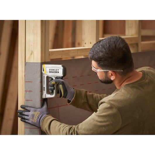 STANLEY FATMAX FMHT70443-0 stapler used by worker wearing gloves attaching sheeting to wooden frame.