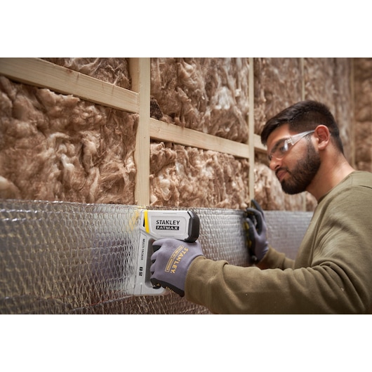 STANLEY FMHT70443-0 stapler in use, fastening insulation material to a wooden wall frame.