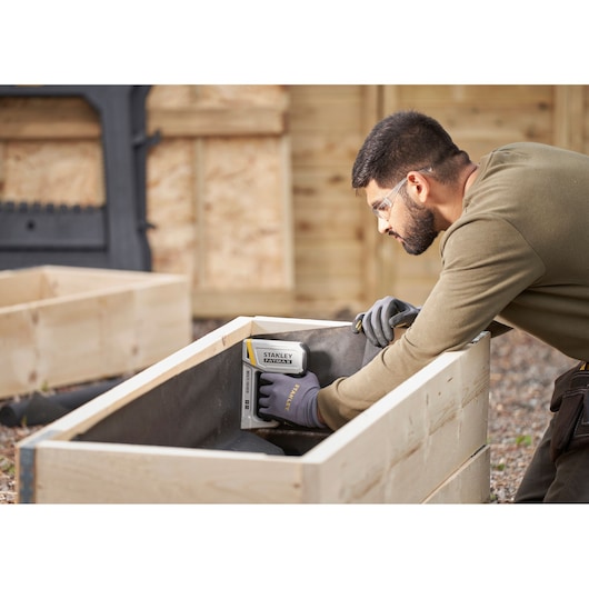 Stanley FMHT70443-0 stapler in use for woodworking, person wearing Stanley gloves outdoors.