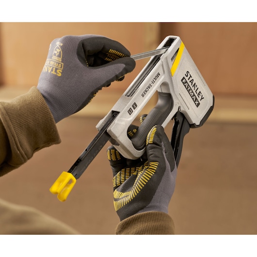 Photo of STANLEY FMHT70443-0 multi-tacker tool loaded with staples, held by gloved hands during use.