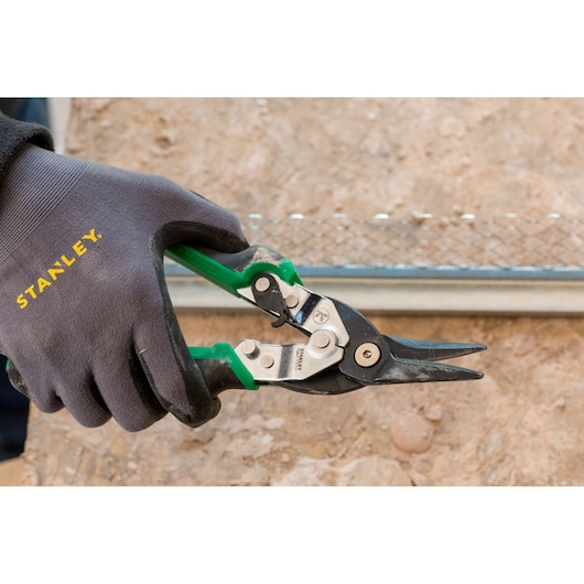 STANLEY FMHT73557-0 aviation snip with green handles held by gloved hand, close-up photo.