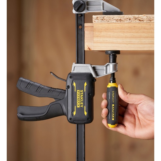 Stanley FMHT83006-0 clamp with black and yellow handle securing wood piece, close-up photography.
