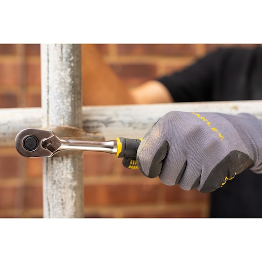 STANLEY FMMT82684-1 ratchet wrench in use on metal pipe, close-up of gloved hand gripping tool.