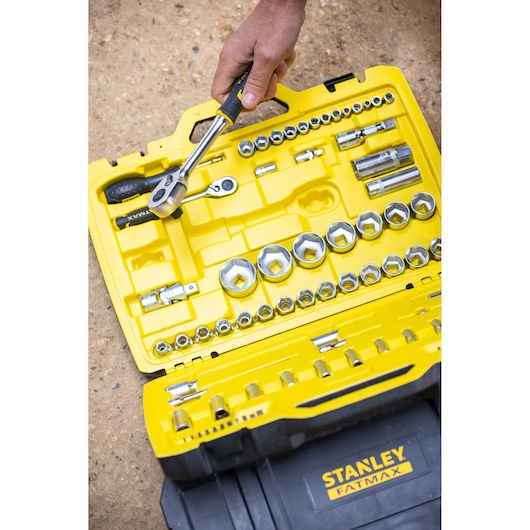 STANLEY FMMT82827-1 socket and ratchet set in yellow and black case, with hand holding ratchet, outdoor setting.