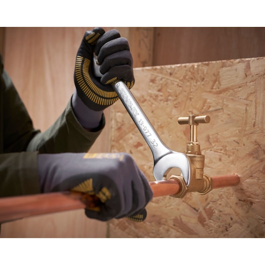 Photo of STANLEY FMMT82902-0 wrench tightening a brass valve on copper pipe, worker wearing gloves.