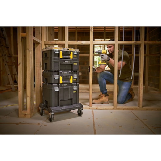 STANLEY FMST1-80107 black stackable toolboxes with yellow handles on wheeled base in a construction site.