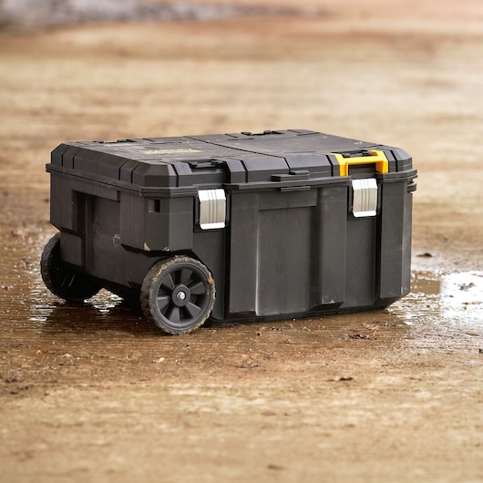 STANLEY FMST17870-1 black wheeled toolbox with yellow handle and metal latches on muddy ground.