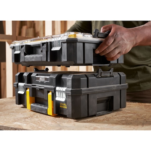 STANLEY FMST82967-1 stackable black toolboxes with yellow latches, person handling upper unit, side angle.