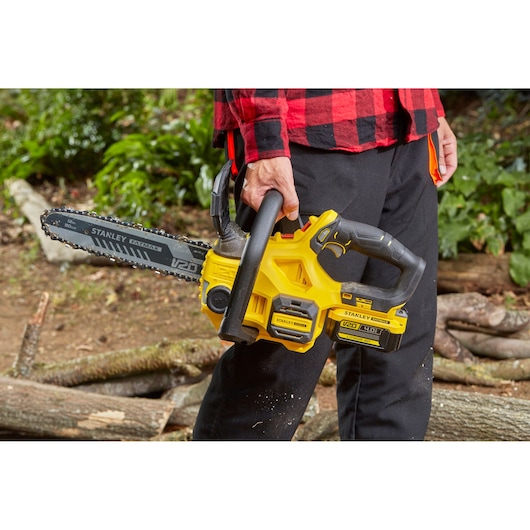 Stanley SFMCCS630B chainsaw held outdoors, yellow and black body, safety grip visible.