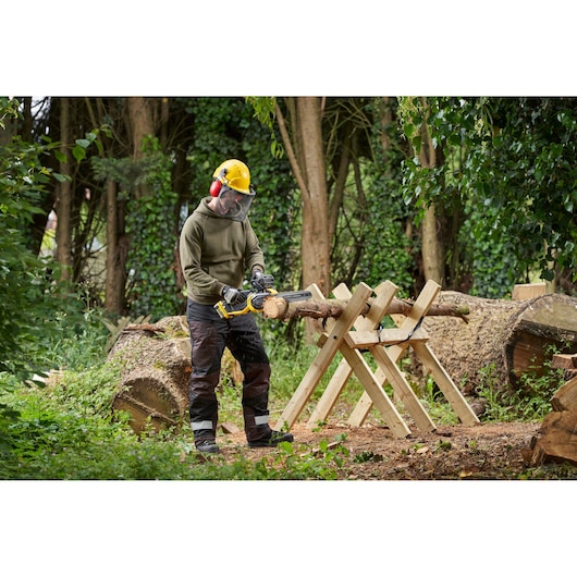 STANLEY SFMCCS730M1 cordless chainsaw in use outdoors cutting a log on a wooden sawhorse.
