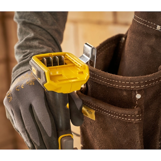 STANLEY SFMCD714D2T drill handle with yellow battery compartment, held by gloved hand near brown tool pouch.
