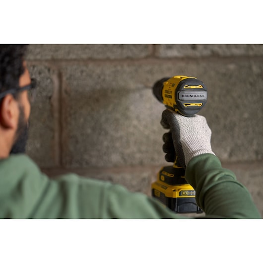 Photo of a person using a STANLEY SFMCD715M2K cordless drill on a concrete wall, close-up side angle.