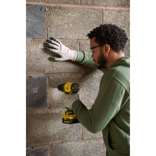 Photo of STANLEY SFMCD715M2K drill used by person in gloves on concrete wall, side angle.