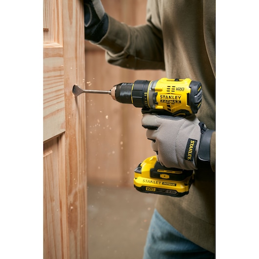 Stanley SFMCD720B cordless drill in use drilling into wood, side angle photography.