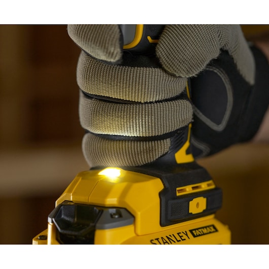 Photo of STANLEY SFMCD721B drill held by gloved hand, LED work light illuminated, close-up view.