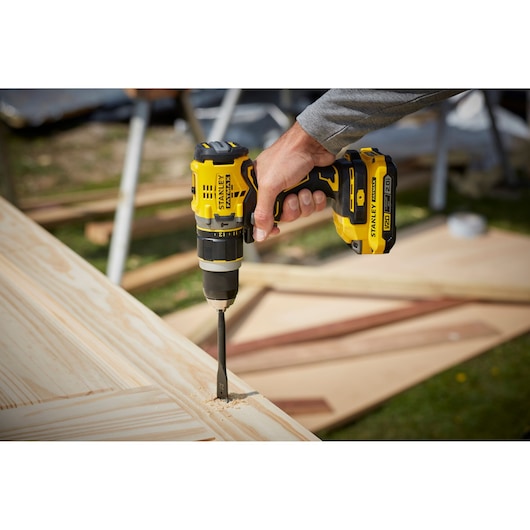 Photo of STANLEY SFMCD721B cordless drill in use on wood, close-up of drilling.