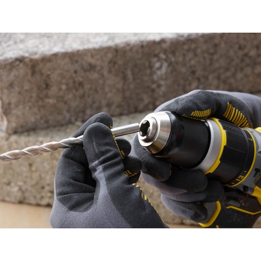 STANLEY SFMCD721D2K drill with gloved hands inserting a metal drill bit, close-up outdoor photography.