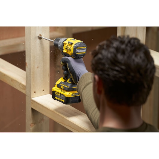 Photo of STANLEY SFMCD725B cordless drill in use drilling into wood, side angle, black and yellow design.
