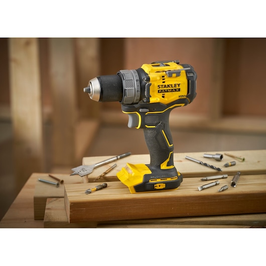 STANLEY SFMCD725B cordless drill in yellow and black, side angle, placed on wooden planks with drill bits