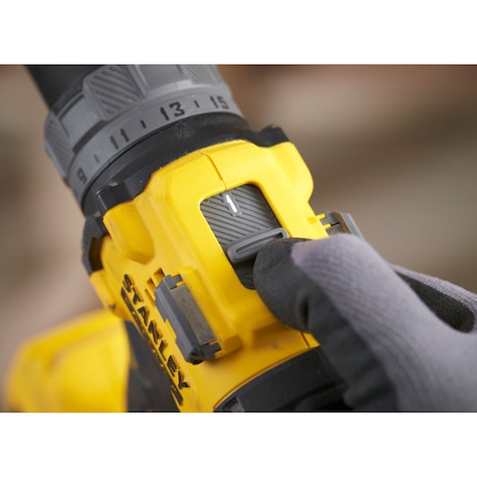 STANLEY SFMCD725B cordless drill speed switch close-up, yellow and black body, gloved hand adjusting.