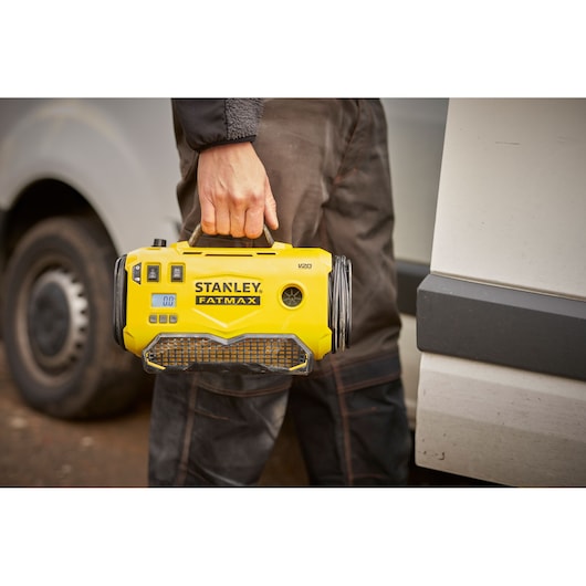Stanley SFMCE520B portable yellow inflator held by handle, taken outdoors near vehicle.