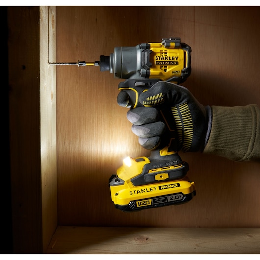 Photo of STANLEY SFMCF830B impact driver in use, yellow and black, side angle, with glove, driving screw into wood.