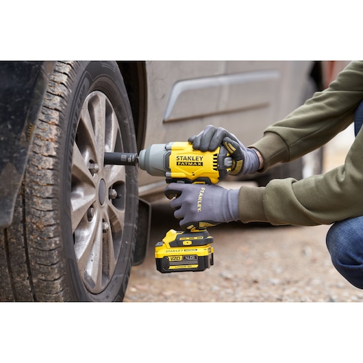 Photo of STANLEY SFMCF940B cordless impact wrench being used to tighten a car wheel lug nut outdoors.