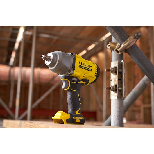 STANLEY SFMCF940B cordless impact wrench, yellow and black, shown upright on wooden surface at construction site.