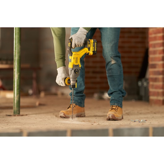STANLEY SFMCH900B rotary hammer drill in use, yellow and black, construction site, photography close-up.
