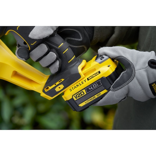 STANLEY SFMCHT855M1 hedge trimmer close-up, user inserting V20 4.0Ah Lithium Ion battery.