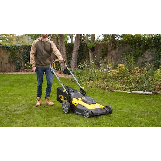 STANLEY SFMCMWS251M lawn mower in use on grass with person holding handle, side garden view.
