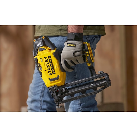 Photo of a person holding a STANLEY SFMCN616B cordless nailer, yellow and black, used for construction tasks.