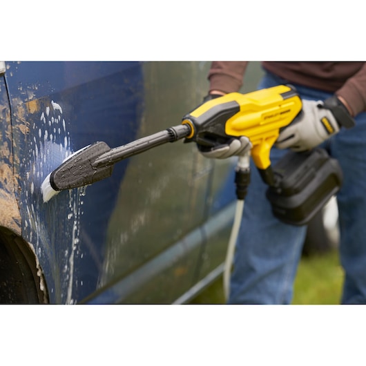 STANLEY SFMCPC93M1 portable power cleaner washing blue car door with soap and brush attachment.