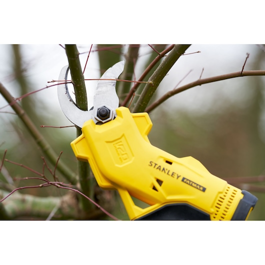 STANLEY SFMCPP32M1 cordless pruner trimming tree branch, close-up outdoor photography.