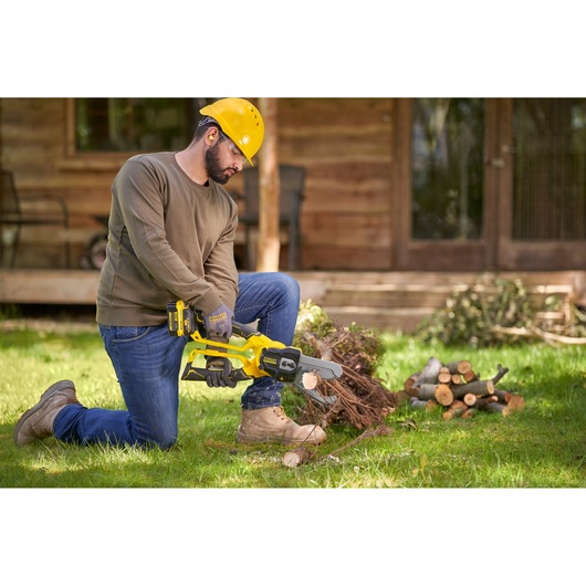 Photo of STANLEY SFMCPS515M1 cordless chainsaw in use, man cutting wood in a garden setting.