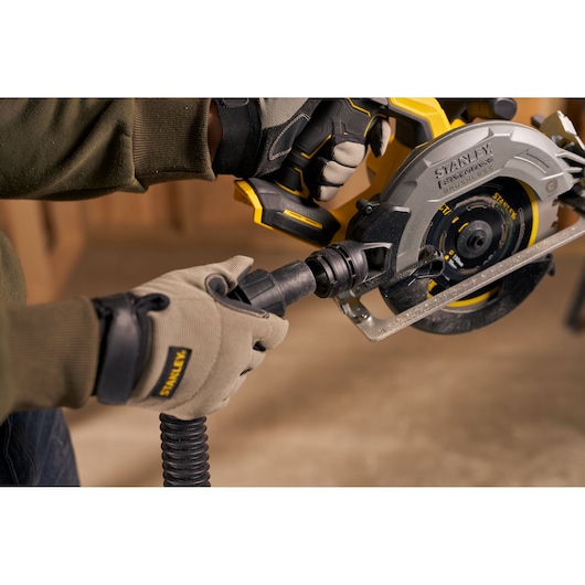 STANLEY SFMCS550B circular saw with vacuum attachment held by gloved hands in workshop setting.