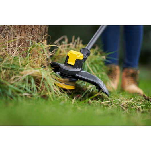 STANLEY SFMCSTB933M grass trimmer close-up cutting grass around tree, yellow and black design.