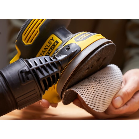 STANLEY SFMCW220B sander held in hand, mesh sanding pad being attached, close-up view.