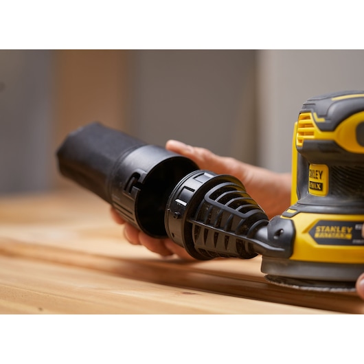 STANLEY SFMCW220B sander with dust collector attachment in close-up, shown on a wooden surface.