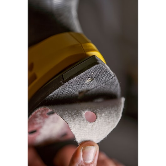 STANLEY SFMCW221B sander with abrasive pad being attached, close-up photography showing yellow and black details.