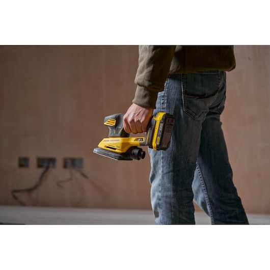 Person holding STANLEY SFMCW221D1S cordless sander, yellow and black, shown in use, product photography.