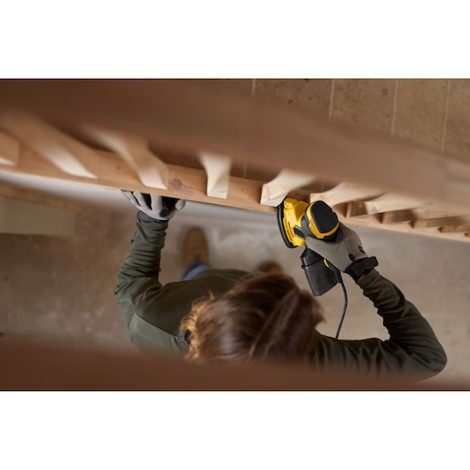 Person using STANLEY SFMEW210S sander on wooden staircase railing, top-down view.