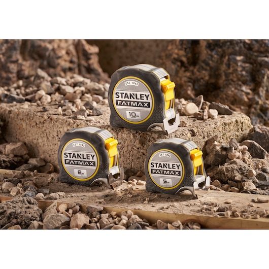 STANLEY FMHT38217-0 FatMax tape measures 5m, 8m, 10m on rocky surface, side angle.