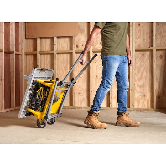 STANLEY SST1800 table saw on wheels being pulled by a person in a construction site, product photography.