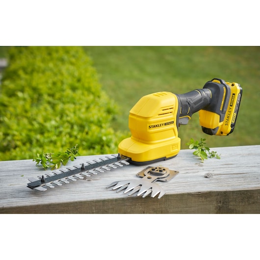 Photo of STANLEY STCSS20B cordless shrub and grass shear with blade attachments on a wooden surface.